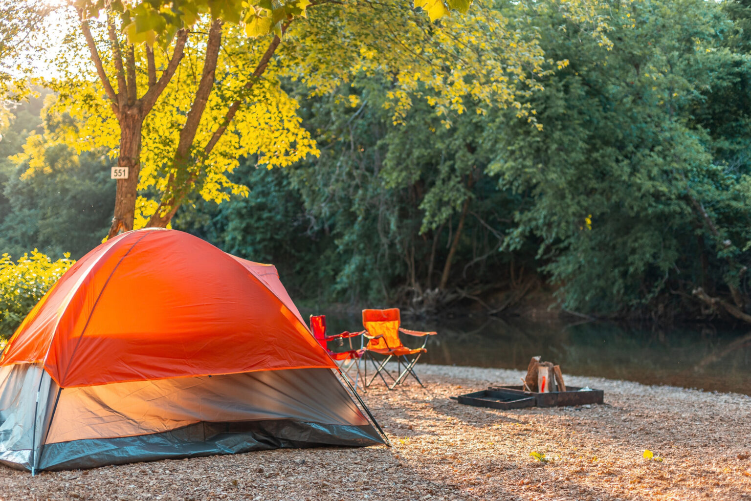 An orange tent and two orange chairs around a campfire.